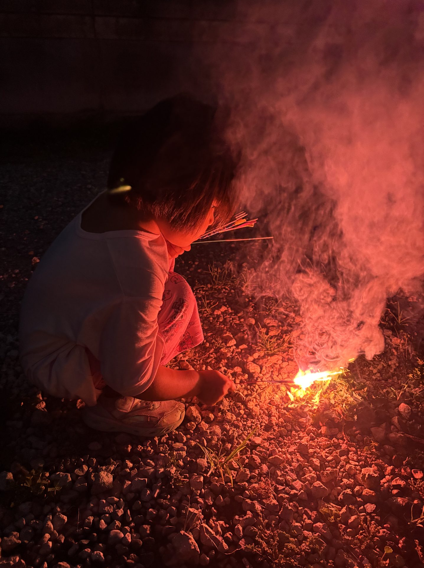 夜、子どもが地面で火をつける様子。小さな火と煙が立ち上る。
